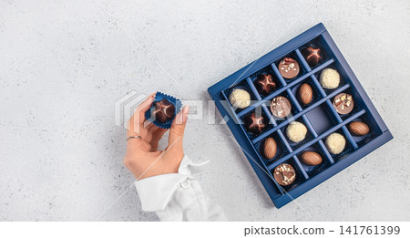 Hand Taking Chocolate from Luxury Assorted Chocolate Gift Box Top View Hand Taking Chocolate from Luxury Assorted Chocolate Gift Box Top View 141761399