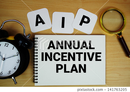 AIP Annual Incentive Plan text written on notepad with magnifying glass and alarm clock on wooden background AIP Annual Incentive Plan text written on notepad with magnifying glass and alarm clock on wooden background 141763205
