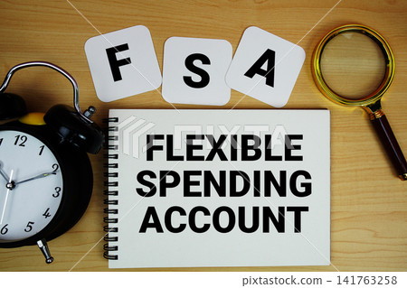 FSA Flexible Spending Account text written on notepad with magnifying glass and alarm clock on wooden background FSA Flexible Spending Account text written on notepad with magnifying glass and alarm clock on wooden background 141763258