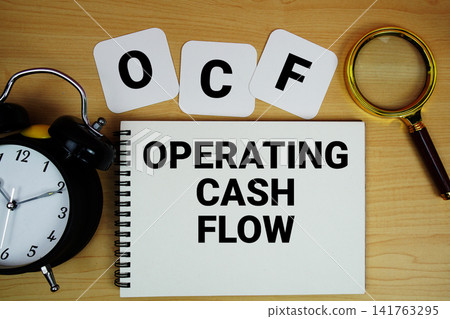OCF Operating Cash Flow text written on notepad with magnifying glass and alarm clock on wooden background OCF Operating Cash Flow text written on notepad with magnifying glass and alarm clock on wooden background 141763295