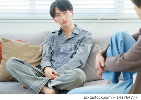 A Japanese man with a serious expression is sitting on a sofa and having a conversation. A Japanese man with a serious expression is sitting on a sofa and having a conversation. 141764777