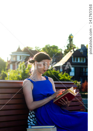 Girl with book under summer trees. Digital detox moment. Brain refreshes with each page. Harmony with surrounding greenery. Simple seasonal joy of outdoor reading Girl with book under summer trees. Digital detox moment. Brain refreshes with each page. Harmony with surrounding greenery. Simple seasonal joy of outdoor reading 141765568