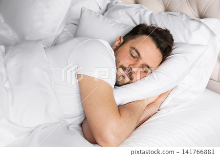 Young adult man sleeping comfortably, while resting on a soft pillow. Concept of healthy sleep, relaxation, wellness, recovery and everyday comfort. Young adult man sleeping comfortably, while resting on a soft pillow. Concept of healthy sleep, relaxation, wellness, recovery and everyday comfort. 141766881