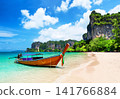 Traditional longtail boat resting on the white sand of Railay Beach near Ao Nang, Thailand. Tropical scenery with turquoise water and dramatic limestone cliffs. 141766884