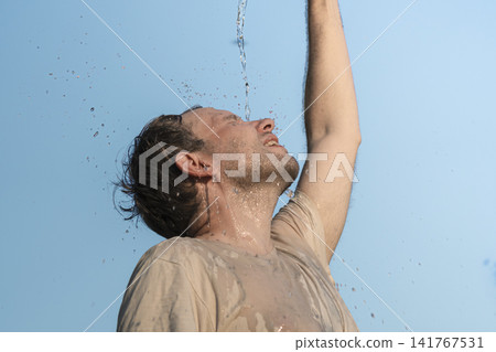 Man pouring water on himself from a blue plastic water bottle outdoors, illustrating heatwave lifestyle adaptations in Europe. Man pouring water on himself from a blue plastic water bottle outdoors, illustrating heatwave lifestyle adaptations in Europe. 141767531