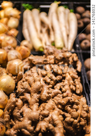 Fresh ginger roots with onions and white radish displayed in supermarket vegetable section with organic produce and healthy cooking ingredients Fresh ginger roots with onions and white radish displayed in supermarket vegetable section with organic produce and healthy cooking ingredients 141768032