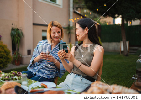 Diverse friends enjoying summer garden party with smartphone Diverse friends enjoying summer garden party with smartphone 141768301