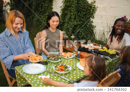 Multi ethnic women and children enjoying backyard barbecue picnic Multi ethnic women and children enjoying backyard barbecue picnic 141768302