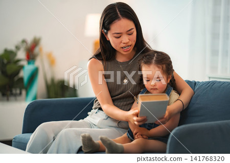 Mother and daughter reading book together at home Mother and daughter reading book together at home 141768320
