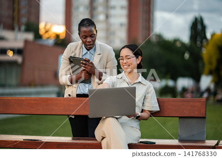 Two businesswomen collaborating on laptop and digital tablet in park Two businesswomen collaborating on laptop and digital tablet in park 141768330
