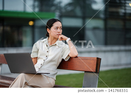 Asian businesswoman contemplating work project outdoors on bench Asian businesswoman contemplating work project outdoors on bench 141768331