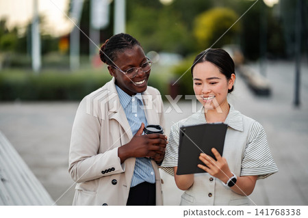 Diverse businesswomen checking tablet, discussing project outdoors Diverse businesswomen checking tablet, discussing project outdoors 141768338