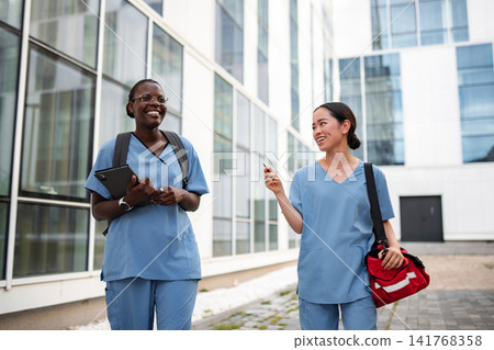 Diverse nurses walking enjoying conversation outside clinic building Diverse nurses walking enjoying conversation outside clinic building 141768358