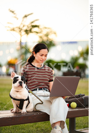 Japanese woman remote working with her French bulldog in park Japanese woman remote working with her French bulldog in park 141768365