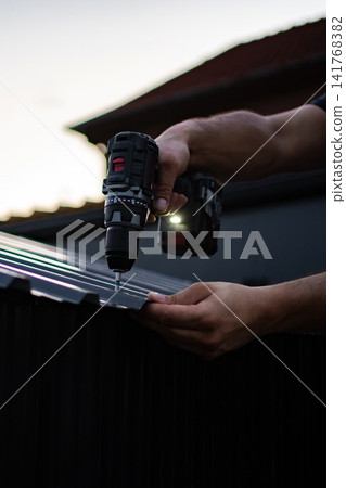 Worker using cordless drill on corrugated metal roof Worker using cordless drill on corrugated metal roof 141768382