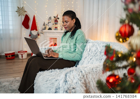 Woman shopping online with laptop in Christmas decorated home Woman shopping online with laptop in Christmas decorated home 141768384