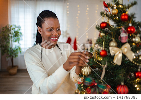 Smiling woman decorating festive Christmas tree with ornaments Smiling woman decorating festive Christmas tree with ornaments 141768385