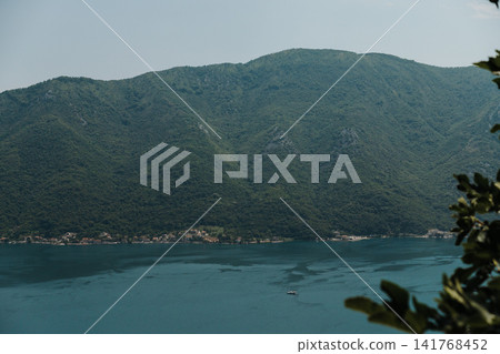 Small hillside village overlooking the Bay of Kotor in Montenegro. Forested mountains and calm Adriatic waters frame the peaceful coastal settlement Small hillside village overlooking the Bay of Kotor in Montenegro. Forested mountains and calm Adriatic waters frame the peaceful coastal settlement 141768452