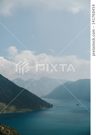 Panoramic view of Perast, the Bay of Kotor and the famous islands in Montenegro. Dramatic mountains surround the calm Adriatic waters on a hazy summer day Panoramic view of Perast, the Bay of Kotor and the famous islands in Montenegro. Dramatic mountains surround the calm Adriatic waters on a hazy summer day 141768454