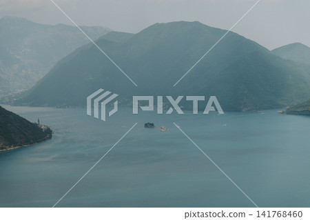 Panoramic view of Perast, the Bay of Kotor and the famous islands in Montenegro. Dramatic mountains surround the calm Adriatic waters on a hazy summer day Panoramic view of Perast, the Bay of Kotor and the famous islands in Montenegro. Dramatic mountains surround the calm Adriatic waters on a hazy summer day 141768460
