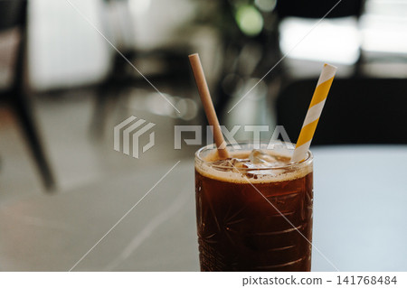 Refreshing iced espresso layered with orange juice served with a paper straw in a modern cafe. Cold specialty coffee beverage on a table Refreshing iced espresso layered with orange juice served with a paper straw in a modern cafe. Cold specialty coffee beverage on a table 141768484