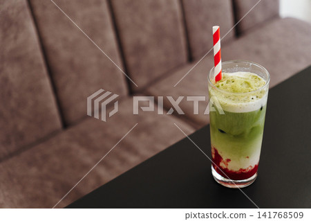 Layered strawberry matcha latte served over ice with creamy foam and a striped paper straw. Refreshing specialty drink presented on a modern cafe table Layered strawberry matcha latte served over ice with creamy foam and a striped paper straw. Refreshing specialty drink presented on a modern cafe table 141768509