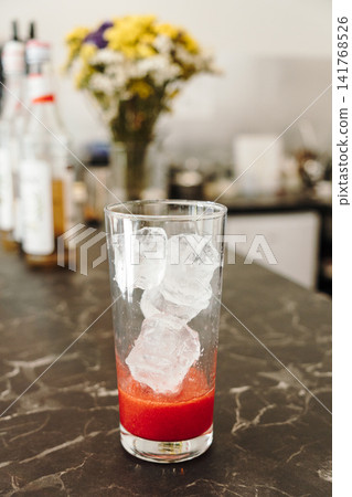 Ice cubes added over fresh strawberry puree inside a serving glass before assembling an iced layered beverage. Refreshing drink preparation in close-up Ice cubes added over fresh strawberry puree inside a serving glass before assembling an iced layered beverage. Refreshing drink preparation in close-up 141768526