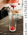 Fresh strawberry puree being poured into a serving glass as the base for a layered iced matcha latte. Colorful drink preparation in a modern cafe 141768528