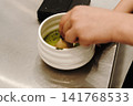 Bamboo whisk mixing matcha tea inside a ceramic bowl to create a smooth texture and foam. Traditional Japanese tea preparation in close-up 141768533
