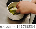 Bamboo whisk mixing matcha tea inside a ceramic bowl to create a smooth texture and foam. Traditional Japanese tea preparation in close-up 141768534