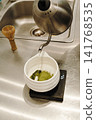 Hot water being poured over sifted matcha powder in a ceramic bowl on a digital scale. Traditional Japanese tea preparation in progress 141768535