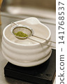 Freshly sifted matcha powder resting in a fine mesh strainer above a ceramic bowl. Traditional tea preparation highlighting premium green tea and brewing equipment 141768537