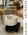 Hands measuring premium matcha powder through a fine mesh strainer into a ceramic bowl. Traditional Japanese tea preparation with precision tools on a digital scale 141768538