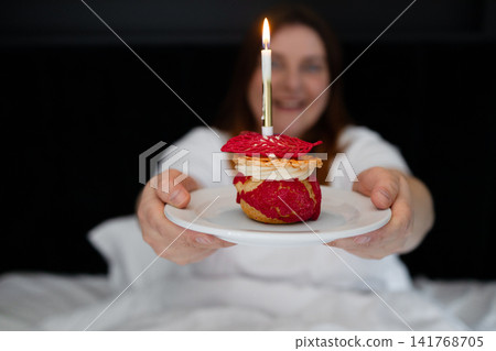 Woman holding a birthday dessert with a burning candle. Woman holding a birthday dessert with a burning candle. 141768705