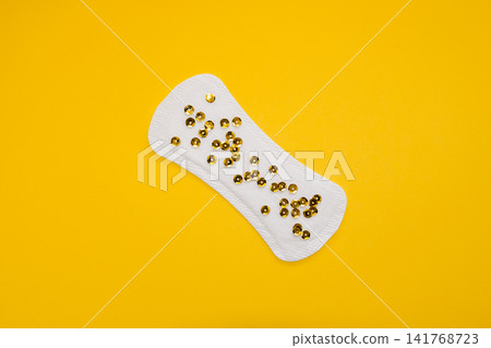 Sanitary Pad with Gold Sequins Representing Urinary Leakage on Yellow Background Sanitary Pad with Gold Sequins Representing Urinary Leakage on Yellow Background 141768723