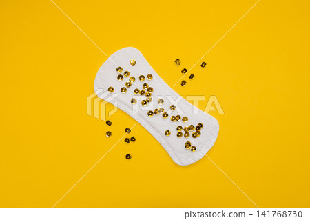 Sanitary Pad with Gold Sequins Representing Urinary Leakage on Yellow Background Sanitary Pad with Gold Sequins Representing Urinary Leakage on Yellow Background 141768730