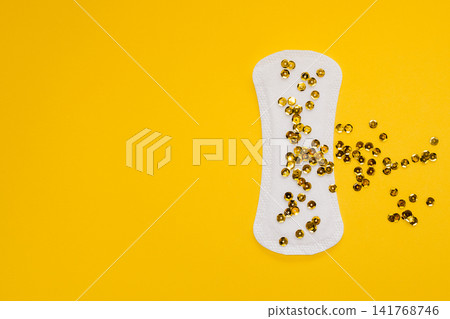 Sanitary Pad with Gold Sequins Representing Urinary Leakage on Yellow Background 141768746