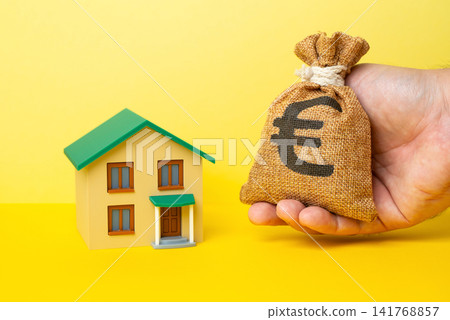 A residential building and a hand holding a euro money bag. Buying a house, investing in real estate. Housing market trends. Home renovation loan. A residential building and a hand holding a euro money bag. Buying a house, investing in real estate. Housing market trends. Home renovation loan. 141768857