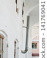 Old building facade with rainwater downspout. Metal rainwater downspout attached to the white facade of an old building with arched architecture.  141769041