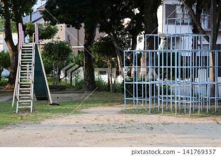 A scene of a park in a residential area with trees, a slide, and a jungle gym. A scene of a park in a residential area with trees, a slide, and a jungle gym. 141769337