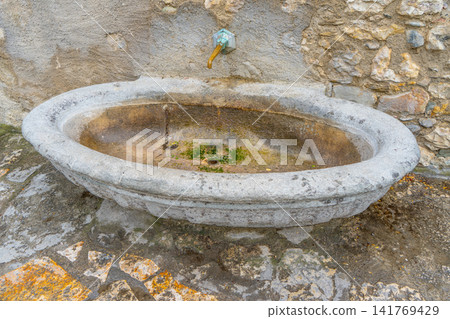Ancient Stone Wall Fountain with Oval Basin and Brass Tap in Old European Village Street Ancient Stone Wall Fountain with Oval Basin and Brass Tap in Old European Village Street 141769429