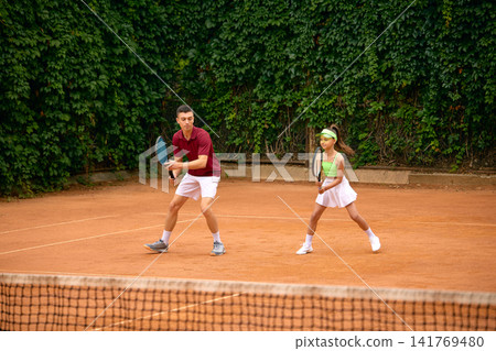 Young girl and male tennis coach practicing ready position together on clay court Young girl and male tennis coach practicing ready position together on clay court 141769480