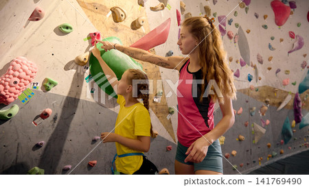 Female coach pointing out climbing hold while teaching young girl indoor bouldering Female coach pointing out climbing hold while teaching young girl indoor bouldering 141769490