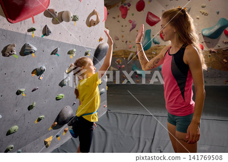Young girl giving high five to female climbing coach after indoor training exercise Young girl giving high five to female climbing coach after indoor training exercise 141769508