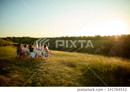 Friends sharing sunset dinner on open Riviera hillside surrounded by nature Friends sharing sunset dinner on open Riviera hillside surrounded by nature 141769552