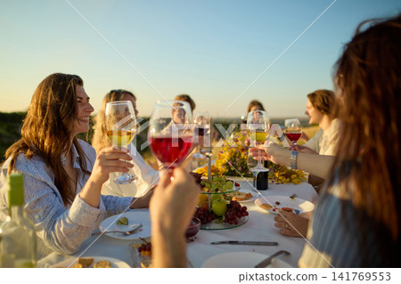 Wine glasses meeting above outdoor table during warm sunset celebration Wine glasses meeting above outdoor table during warm sunset celebration 141769553