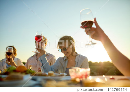 Hands raising wine glasses toward sunlight during lively outdoor group toast 141769554