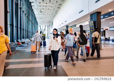 Adult woman scrolling phone while pulling luggage in airport 141769628