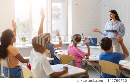 Diverse group of schoolchildren raising hands to answer teachers question during class Diverse group of schoolchildren raising hands to answer teachers question during class 141769710
