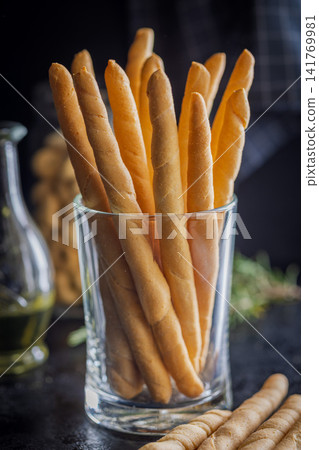 Crunchy Italian Breadsticks (Grissini) In Glass With Herbs, Olive Oil And Jarred Snacks On Wooden Table Crunchy Italian Breadsticks (Grissini) In Glass With Herbs, Olive Oil And Jarred Snacks On Wooden Table 141769981